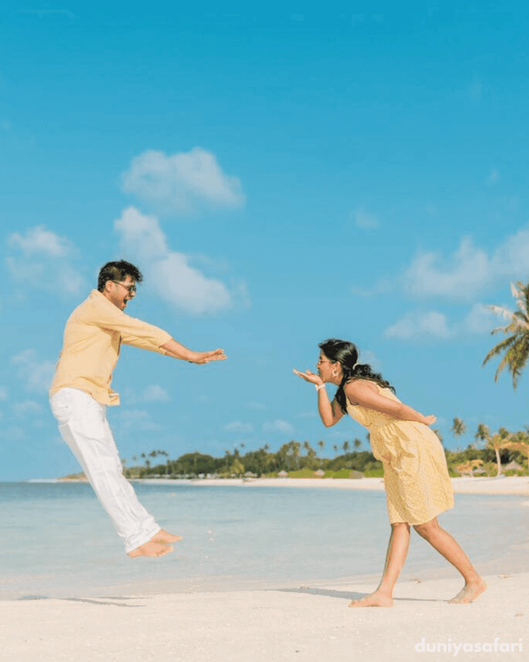 Couple playfully posing on the beach at Atmosphere Kanifushi with turquoise water and palm trees in the background